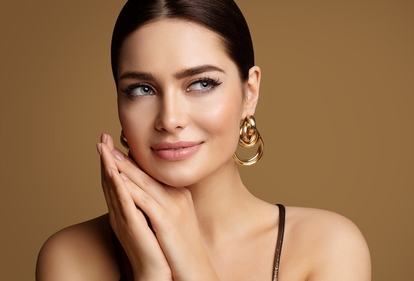 woman with brunette hair up in a bun with makeup and gold hoop earrings.