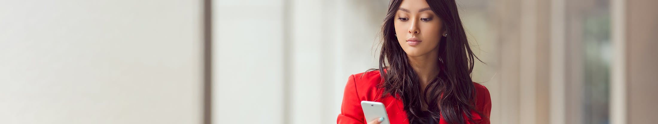 a woman with dark hair looking at her phone wearing a red blazer