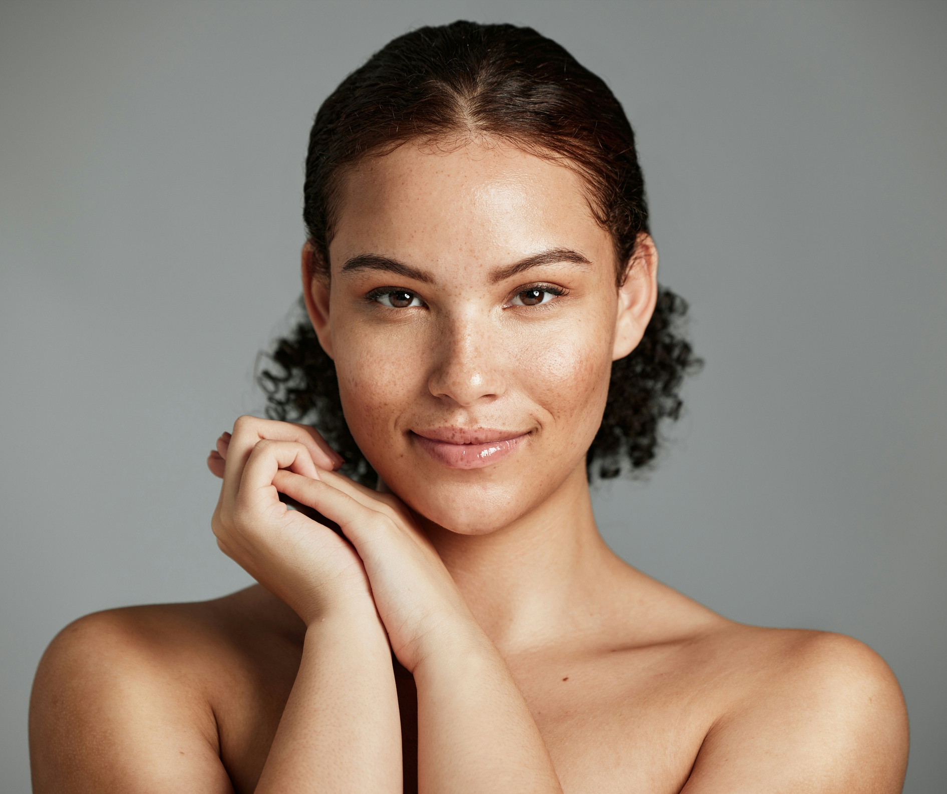 Woman smiling and holding hands together near face
