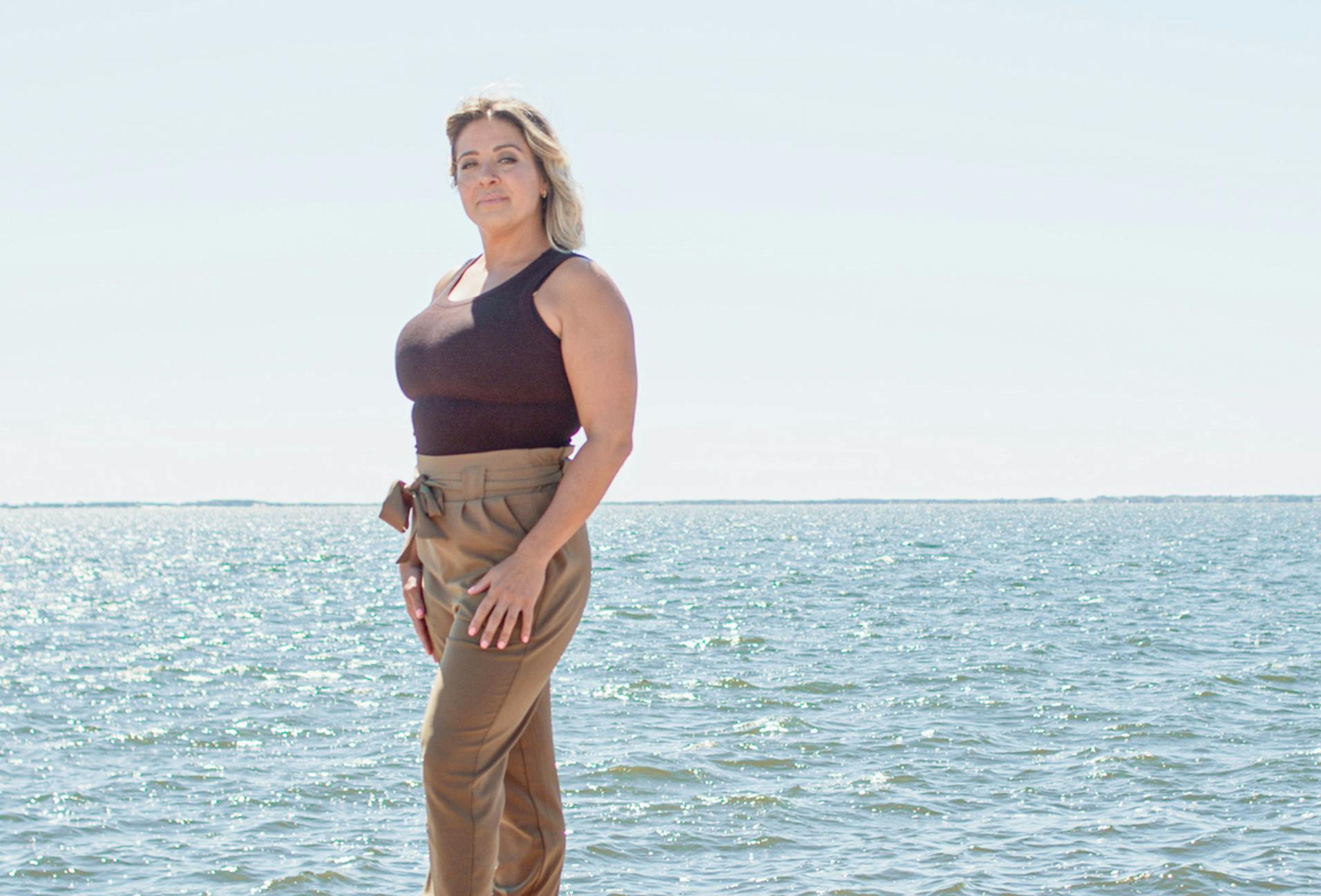 Woman standing by ocean in brown top and pants