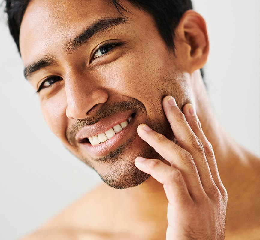 smiling man with his hand touching his cheek while looking at the camera