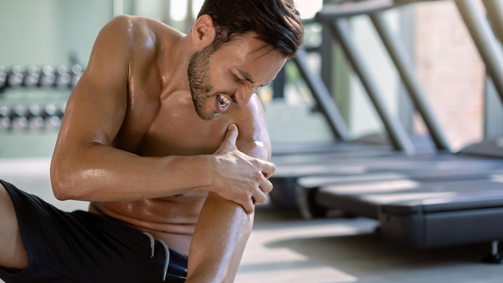 Bild von einen Mann im Gym, der Schmerzen aufgrund von Muskelkater hat.