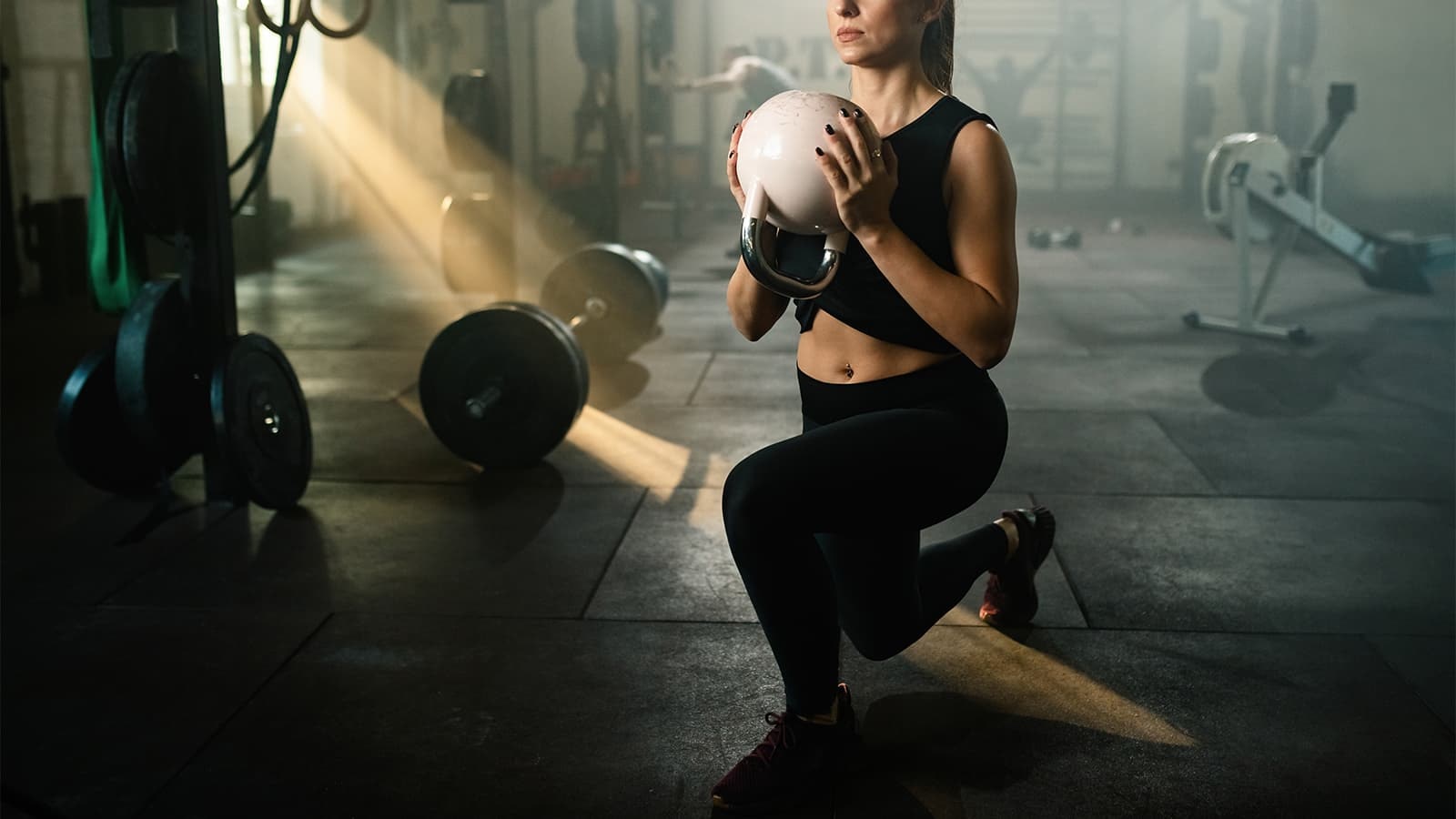 Was genau ist Hyrox? Bild von einer Frau, die eine Kettlebell anhebt, um für Hyrox zu trainieren.