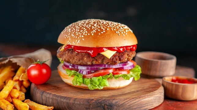 Wie viele Kalorien hat ein Burger? Bild von einem Burger auf einem Holzbrett neben ein paar Beilagen.