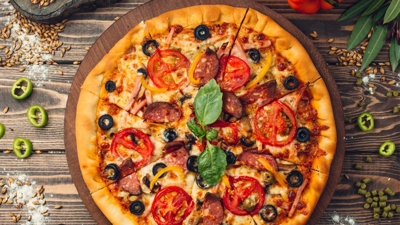 Wie viele Kalorien hat eine Pizza? Bild von einer Pizza auf einem Holzbrett mit ein paar anderen Zutaten.