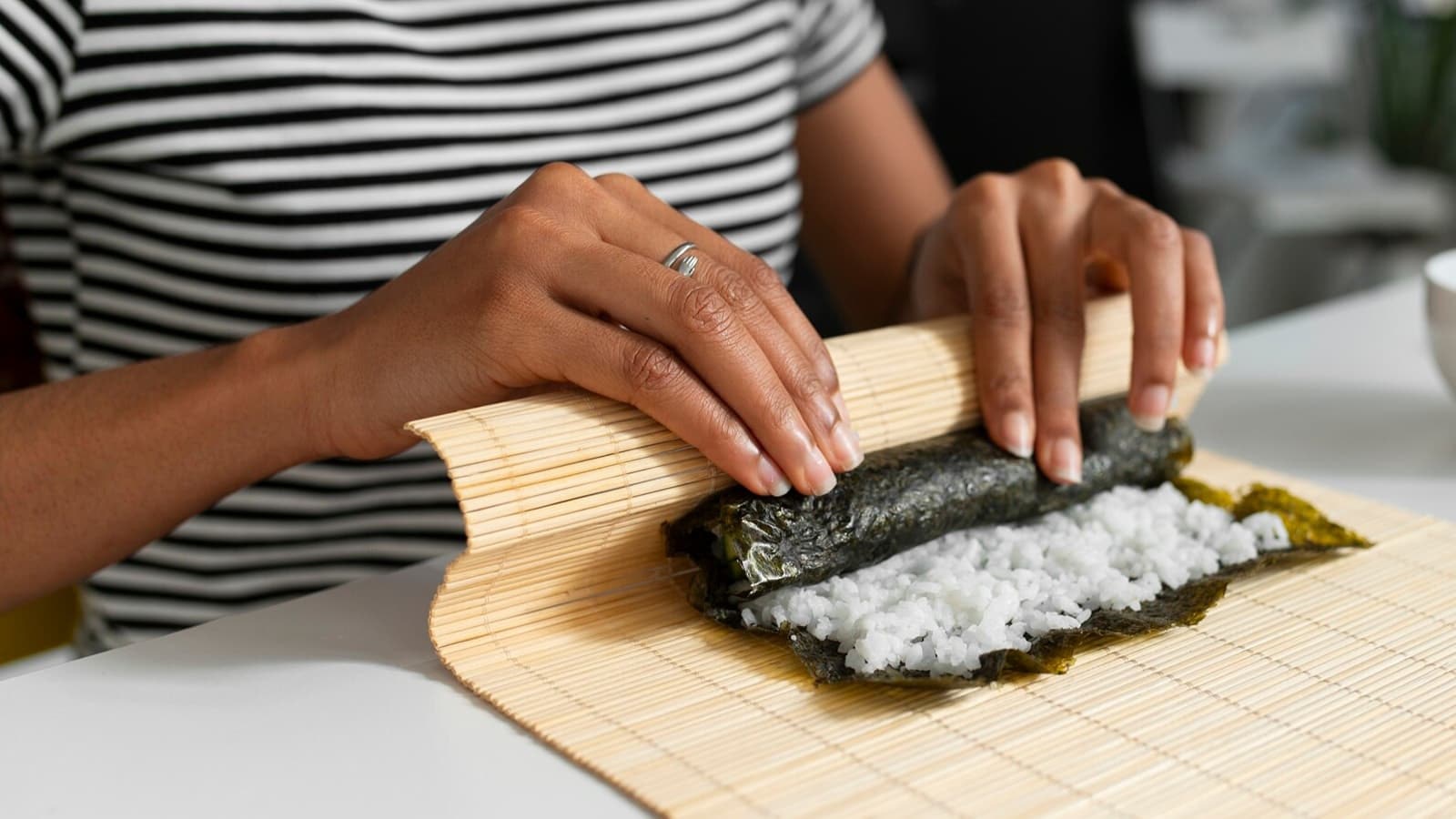 Sushi einfach selbst machen. Bild von einer Frau mit einer Bambusmatte, die benötigt wird, um Sushi zu rollen.