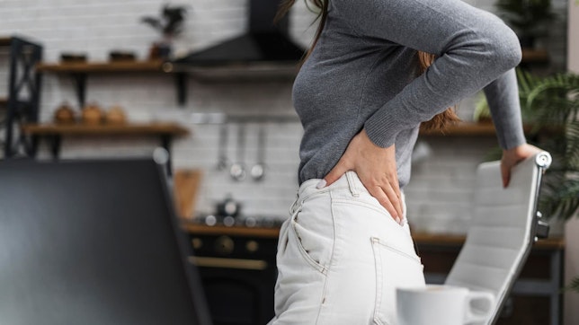 Die besten Übungen gegen Rückenschmerzen. Bild von einer Frau, die Rückenschmerzen vom Sitzen hat.