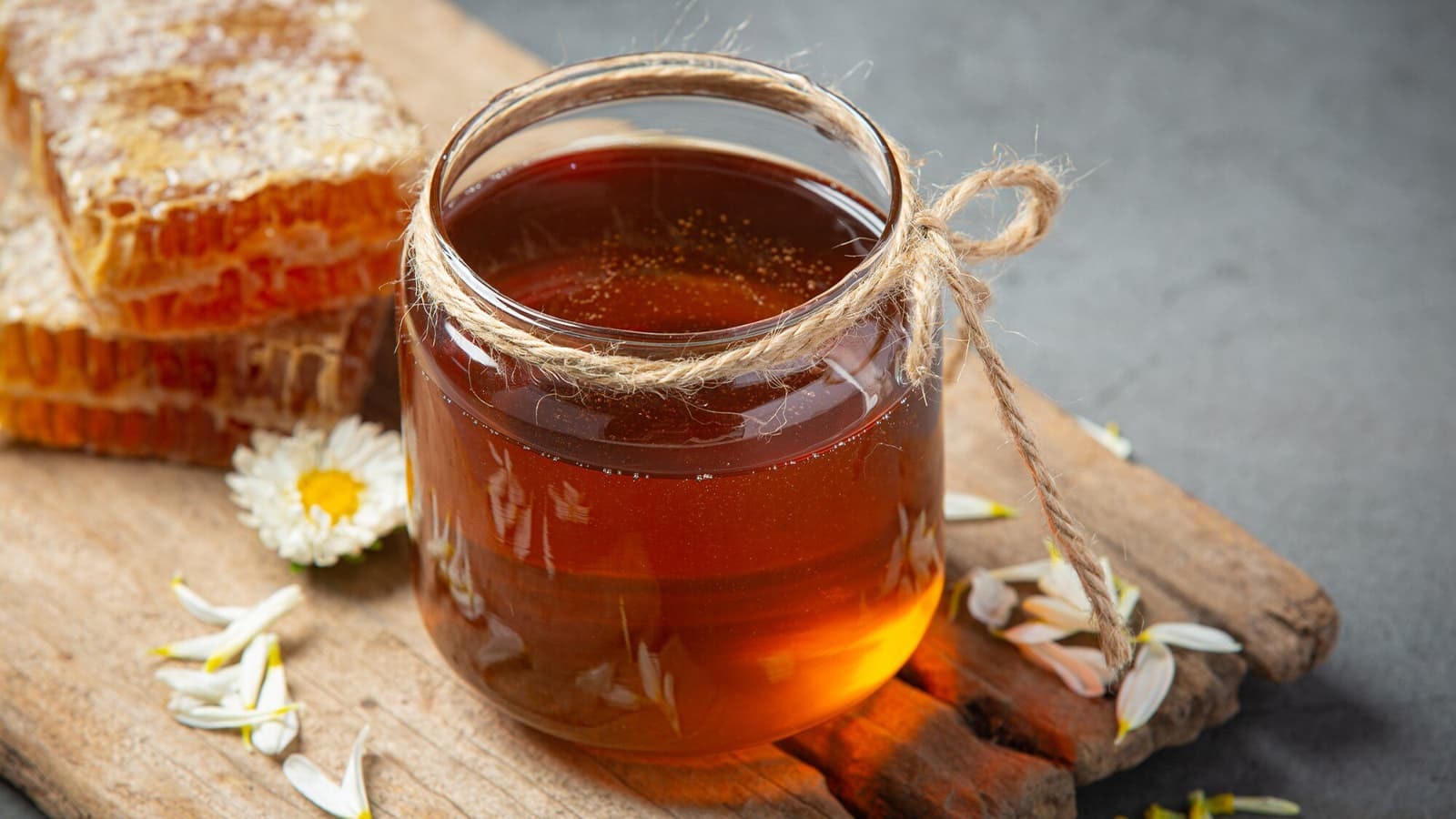 Wie gesund ist eigentlich Honig? Bild von einem Glas mit Honig auf einem Holzbrett.