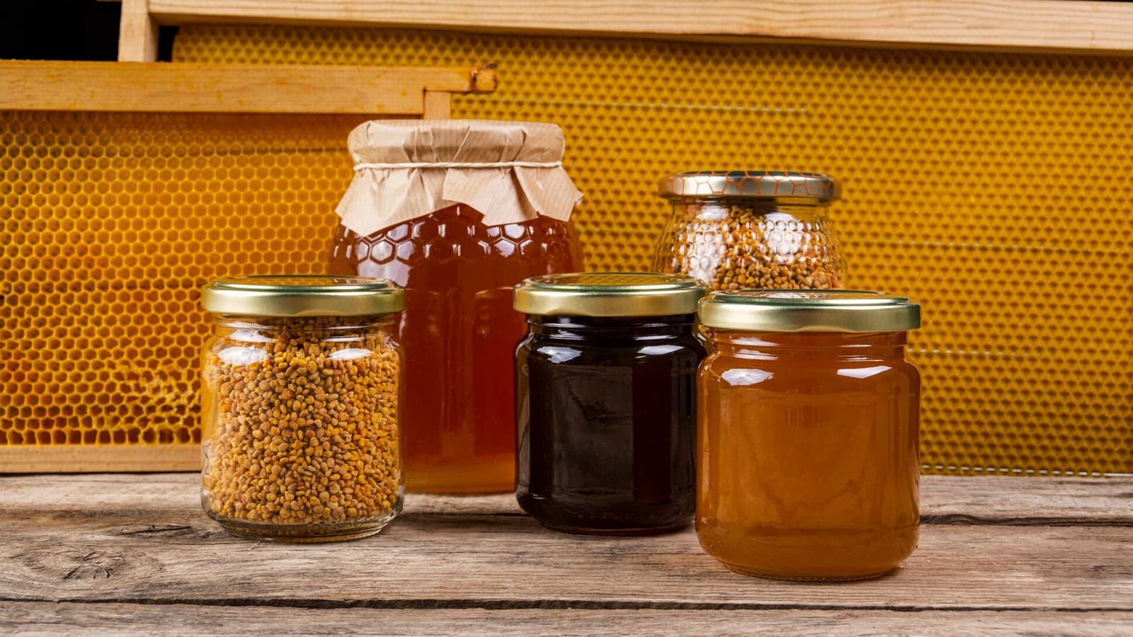 Wie gesund ist eigentlich Honig? Bild von mehreren Gläsern mit Honig vor einer Bienenwabe.