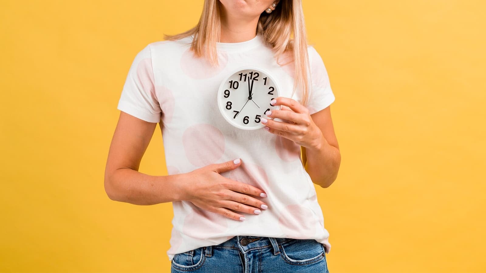 Eine Frau mit einer Uhr in der Hand und der anderen Hand am Bauch.