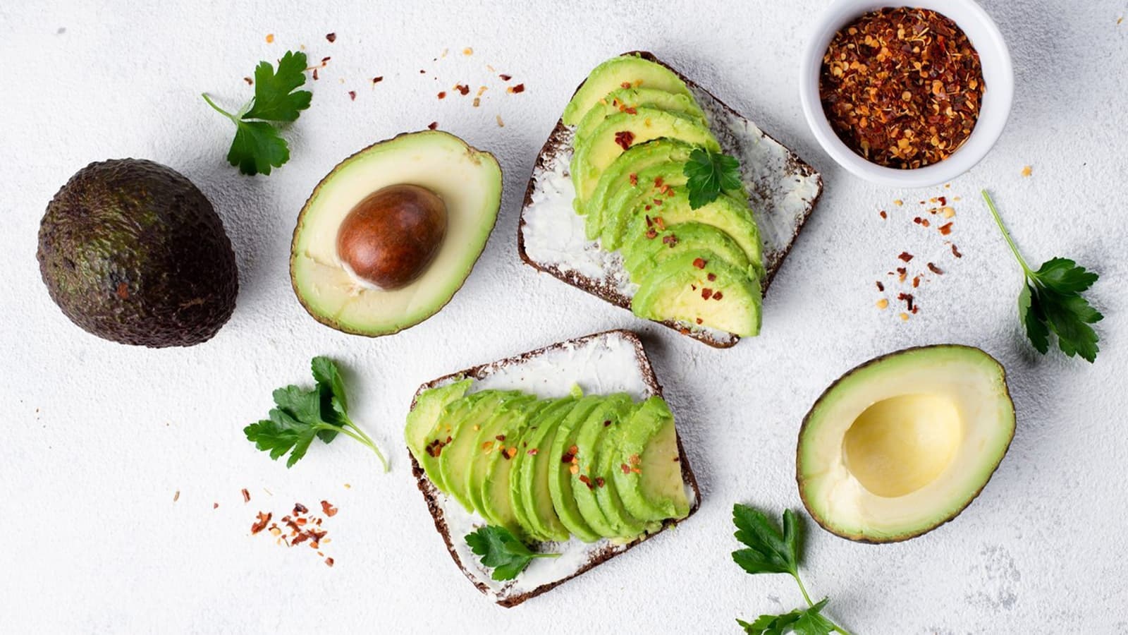Brote belegt mit Avocadoscheiben neben drei halbierten Avocados.