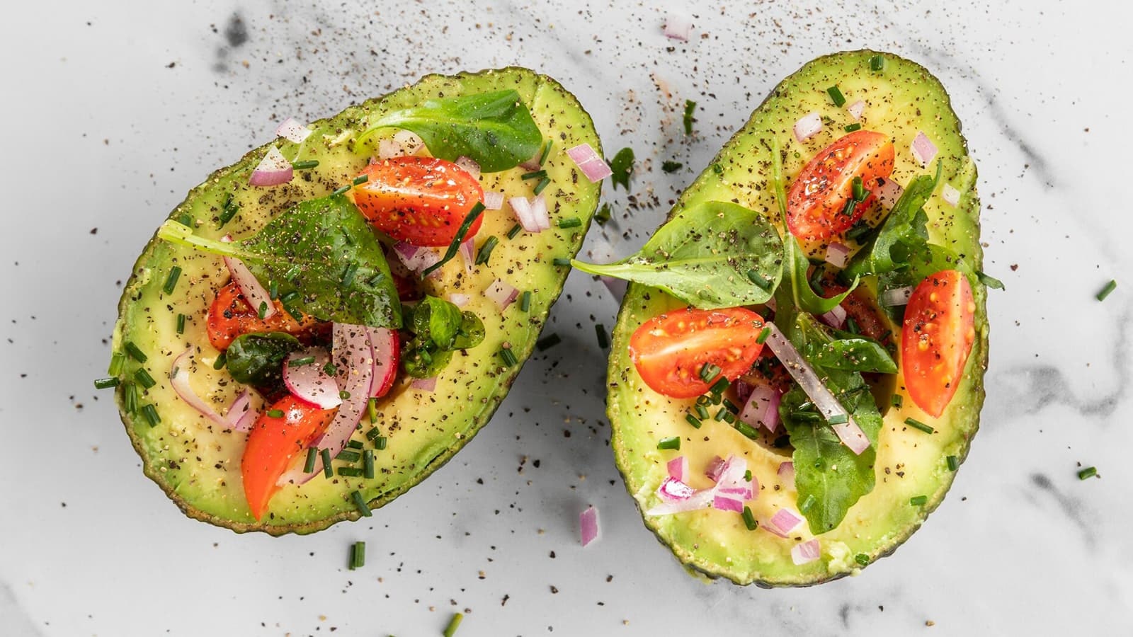 Eine halbierte Avocado gefüllt mit Tomaten, Zwiebeln und Gewürzen.