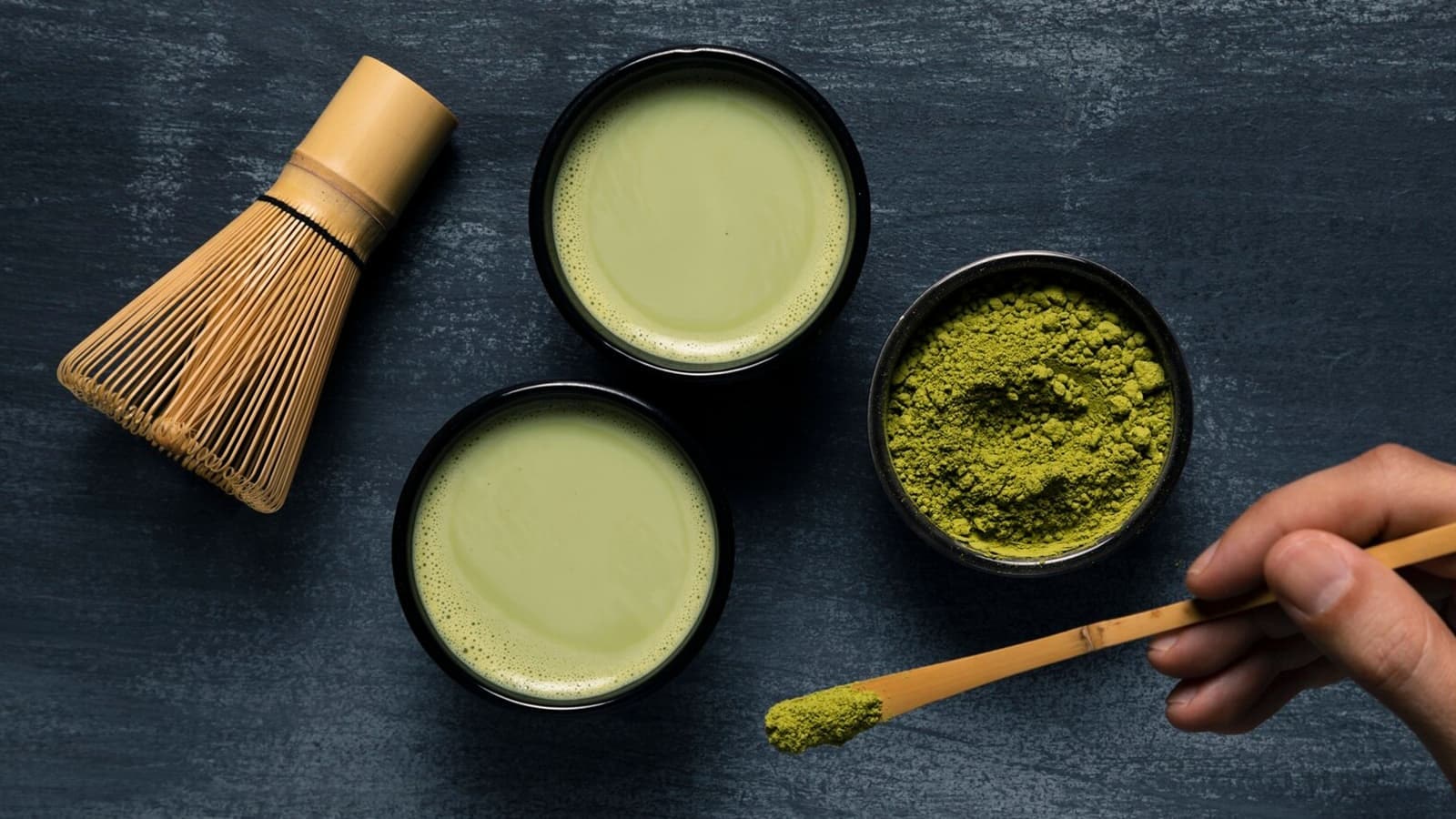 Schalen mit Matcha-Tee und Matcha-Pulver auf dunklem Boden.