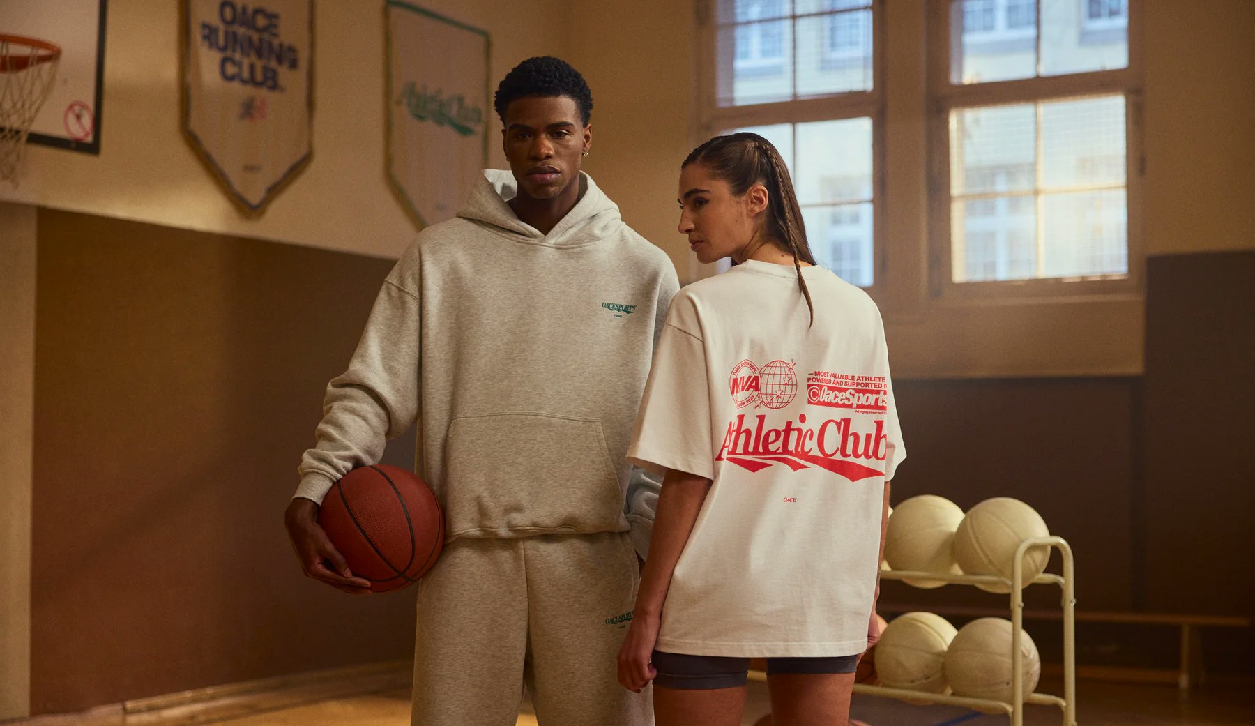 Ein Mann und eine Frau in einer Sporthalle mit Basketball in der Hand. Gekleidet in der neuen OACE Signiture Kollektion.
