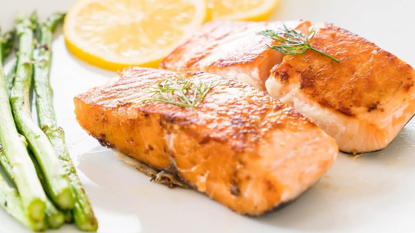Lachsfilets, Spargel und Zitrone auf einem weißen Teller.