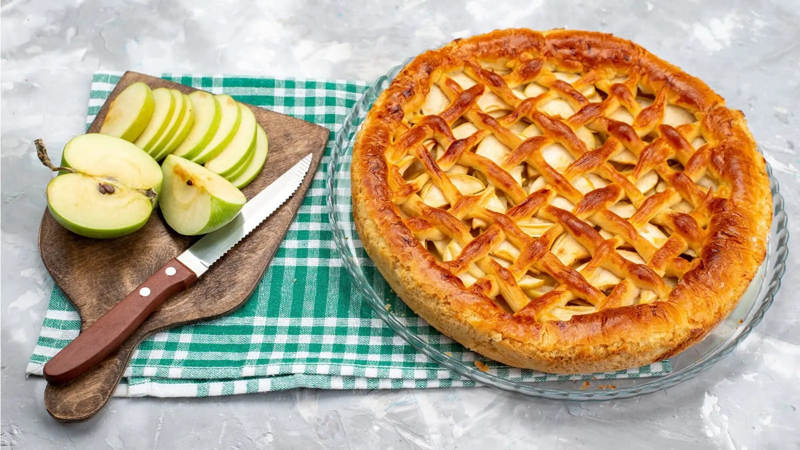 Ein Apfelkuchen neben einem Schneidebrett mit einem Apfel.