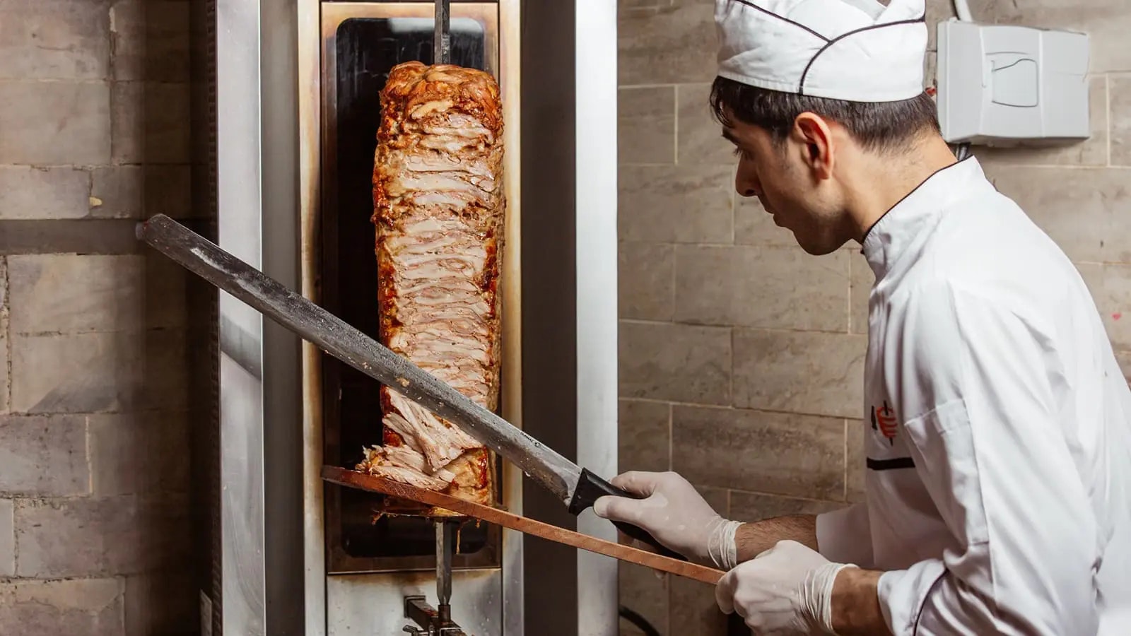 Ein Mann, der Fleisch von einem Dönerspieß schneidet.