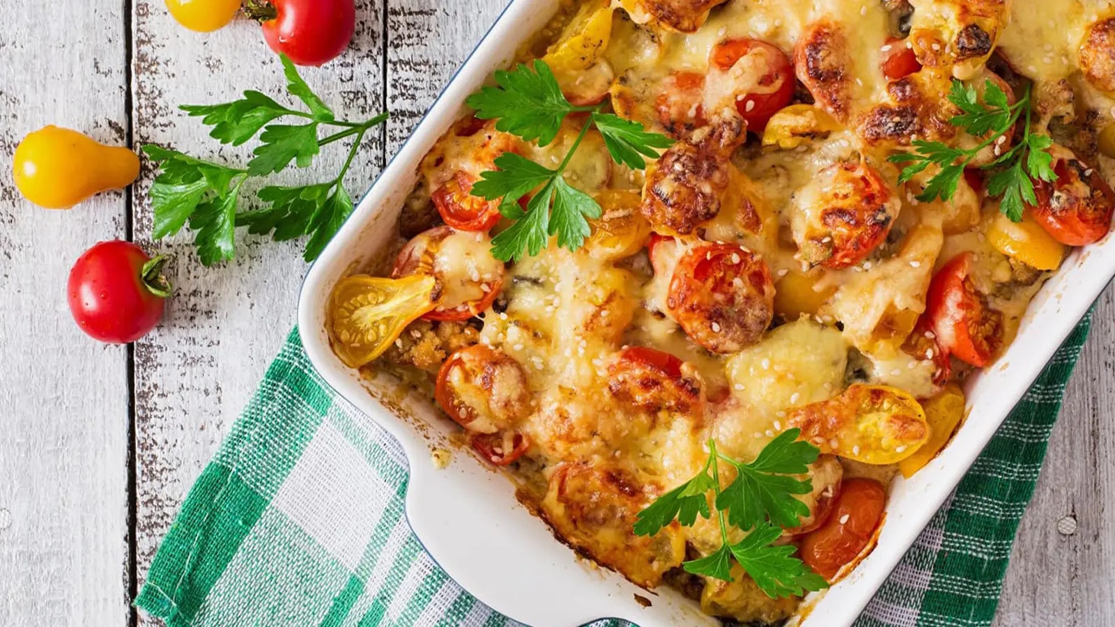 Ein Auflauf, Tomaten und Kräuter auf einem Holztisch.