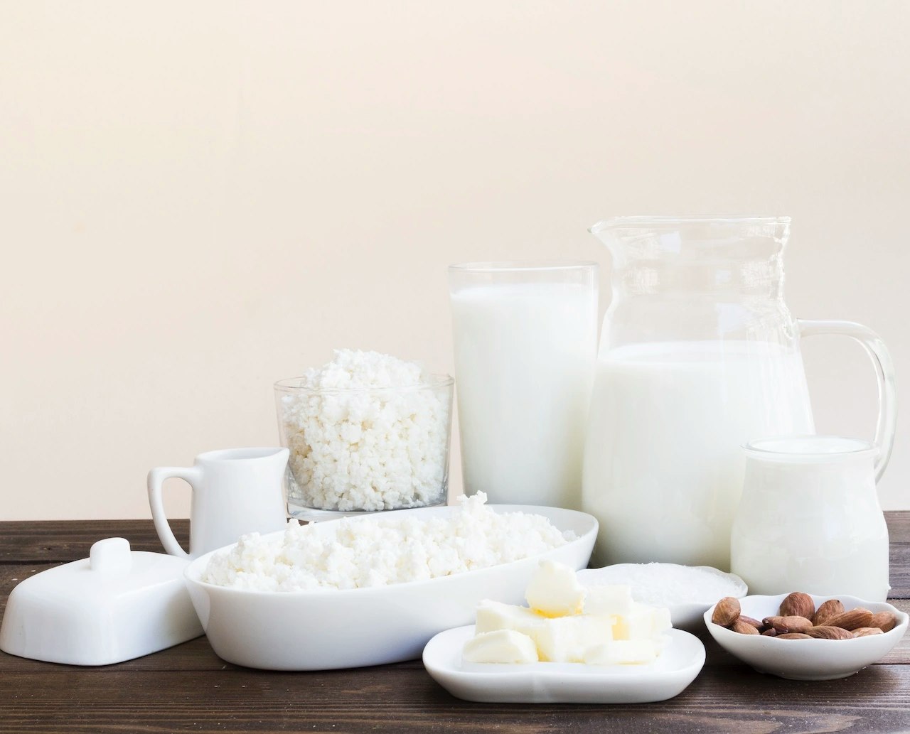 Milch und Milchprodukte wie Frischkäse, Sahne und Mandeln auf einem Holztisch.