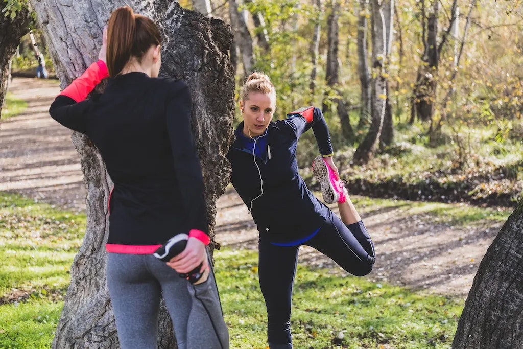 Zwei Frauen, die sich im Wald vor dem Laufen dehnen.