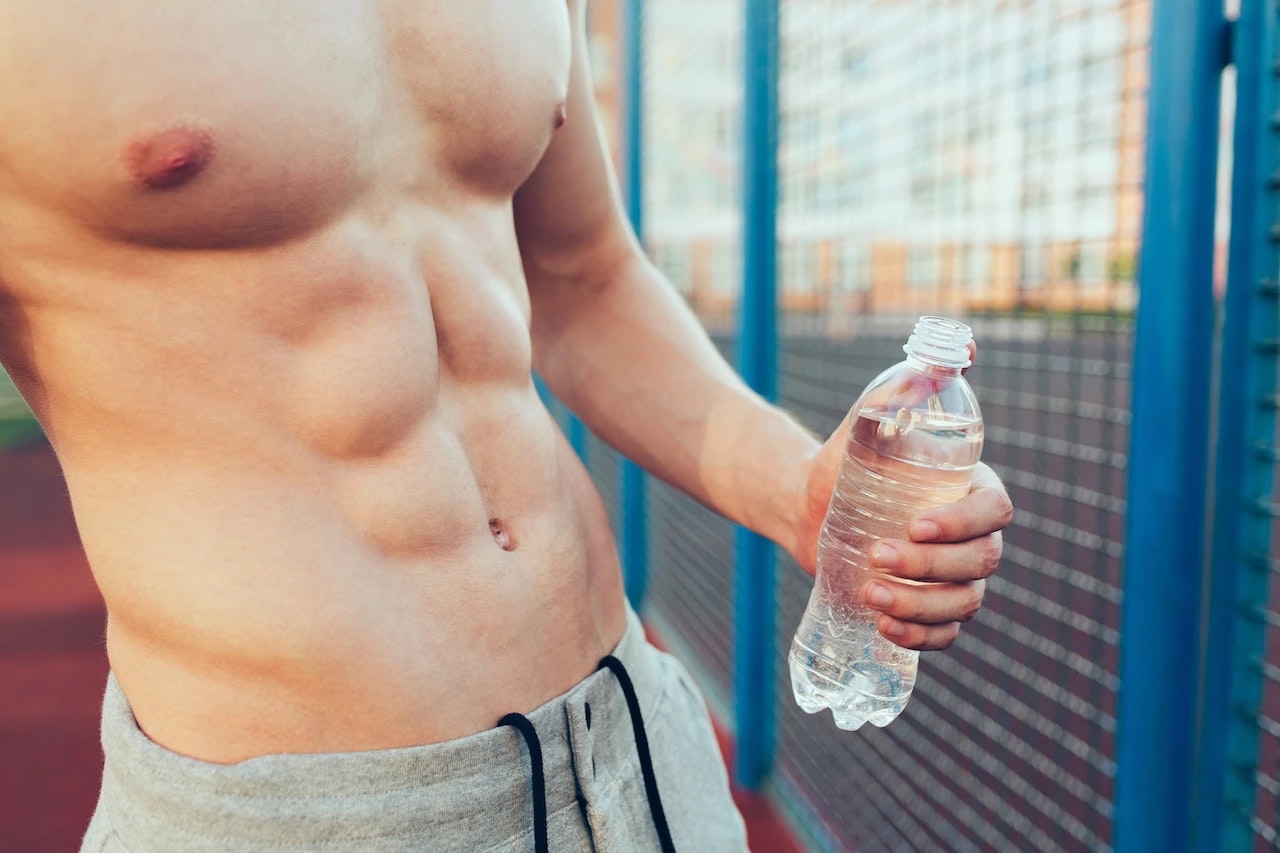 Mann mit Sixpack, Flasche wasser in der Hand auf dem Sportplatz