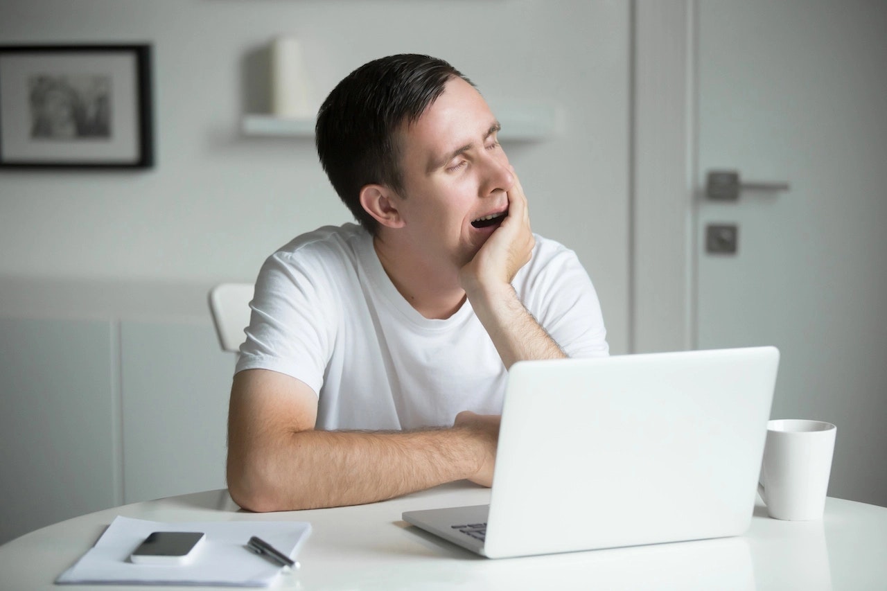 Junger Mann sitzt vor einem Laptop und ist Müde, durch Schlafmangel.