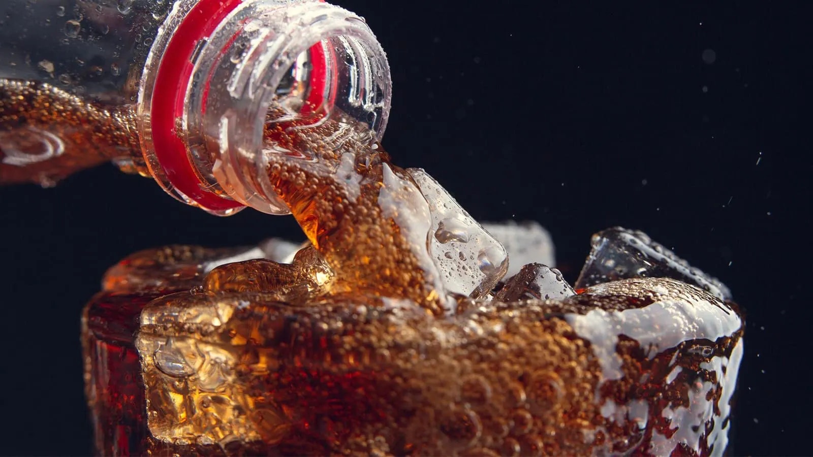 Bild von einem Glas mit Eiswürfeln, welches mit Cola gefüllt wird.