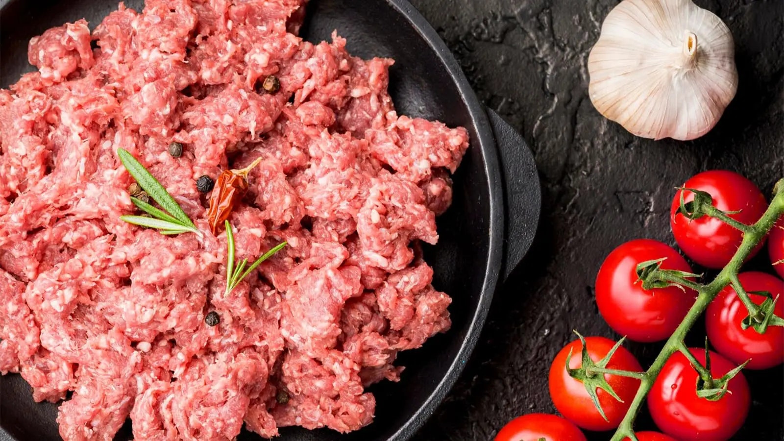 Unverarbeitetes Fleisch in einer Schüssel und Tomaten.