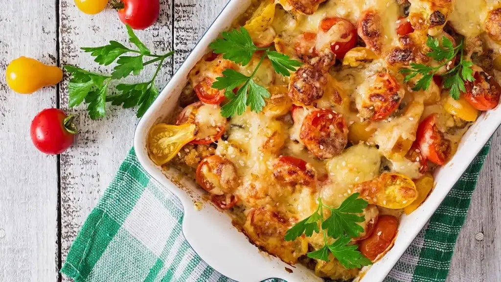 Ein Auflauf, Tomaten und Kräuter auf einem Holztisch.