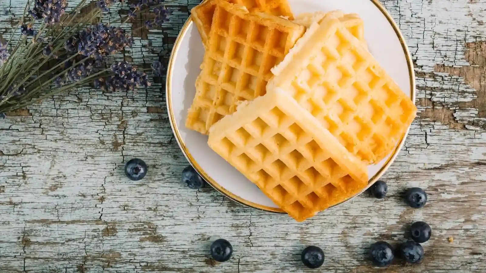 Waffeln auf einem Teller neben ein paar Kräutern und Blaubeeren.