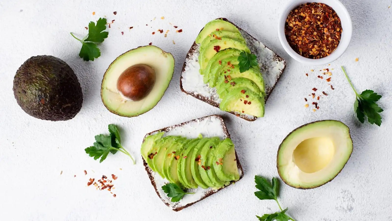 Brote belegt mit Avocadoscheiben neben drei halbierten Avocados.