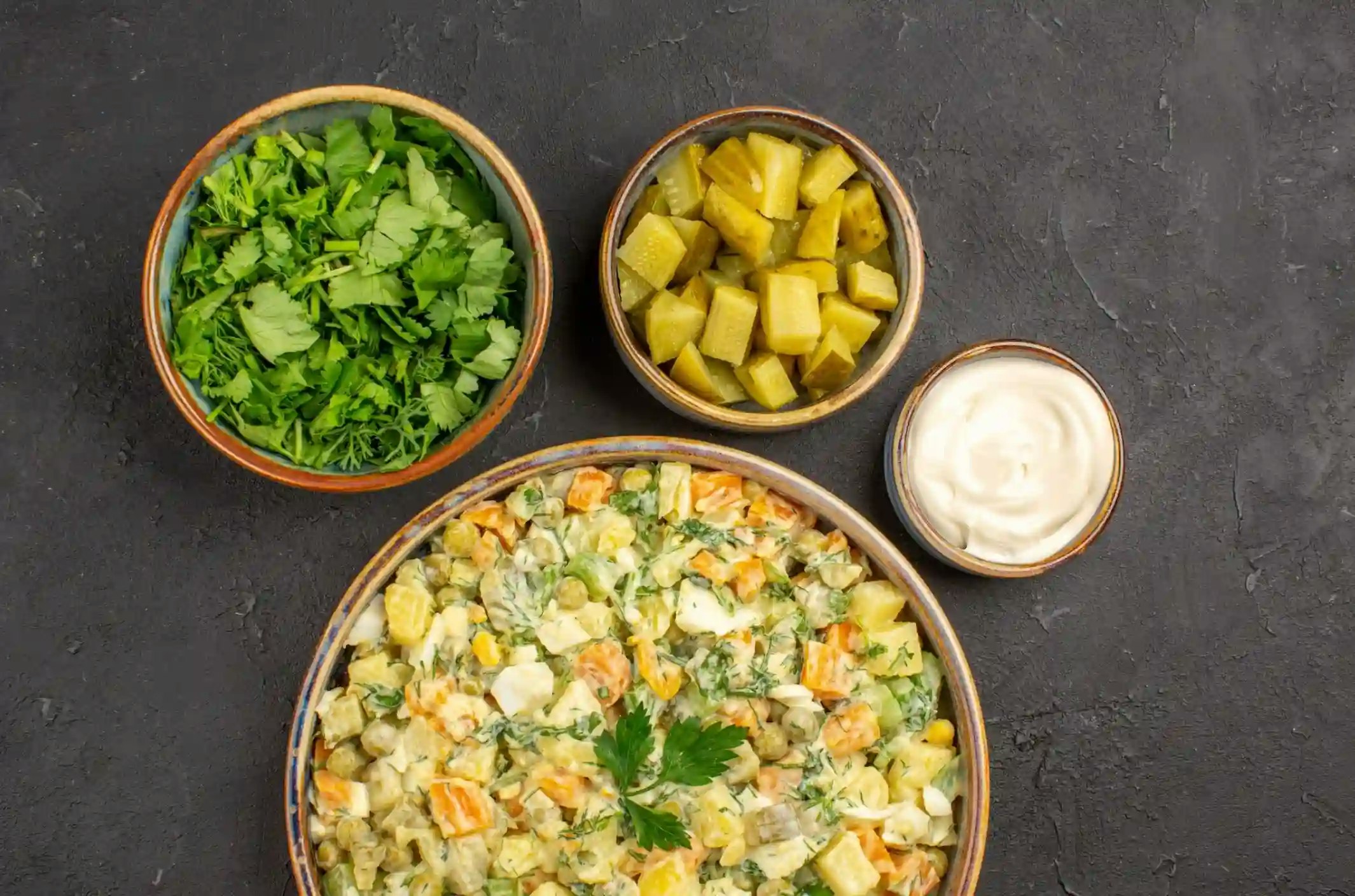 Protein Kartoffelsalat in einer Schale, dazu stehen Petersilie, Gewürugurken und Majonnaise in einer kleinen Schale daneben.