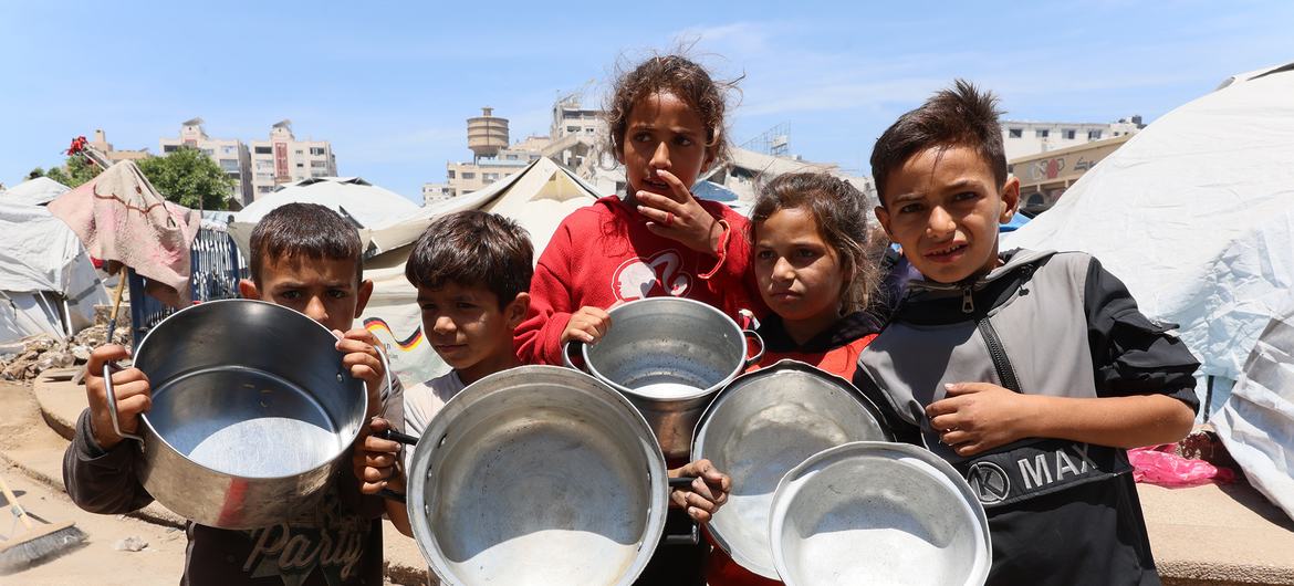 UN News Children in Gaza waiting to have their empty containers filled with food.