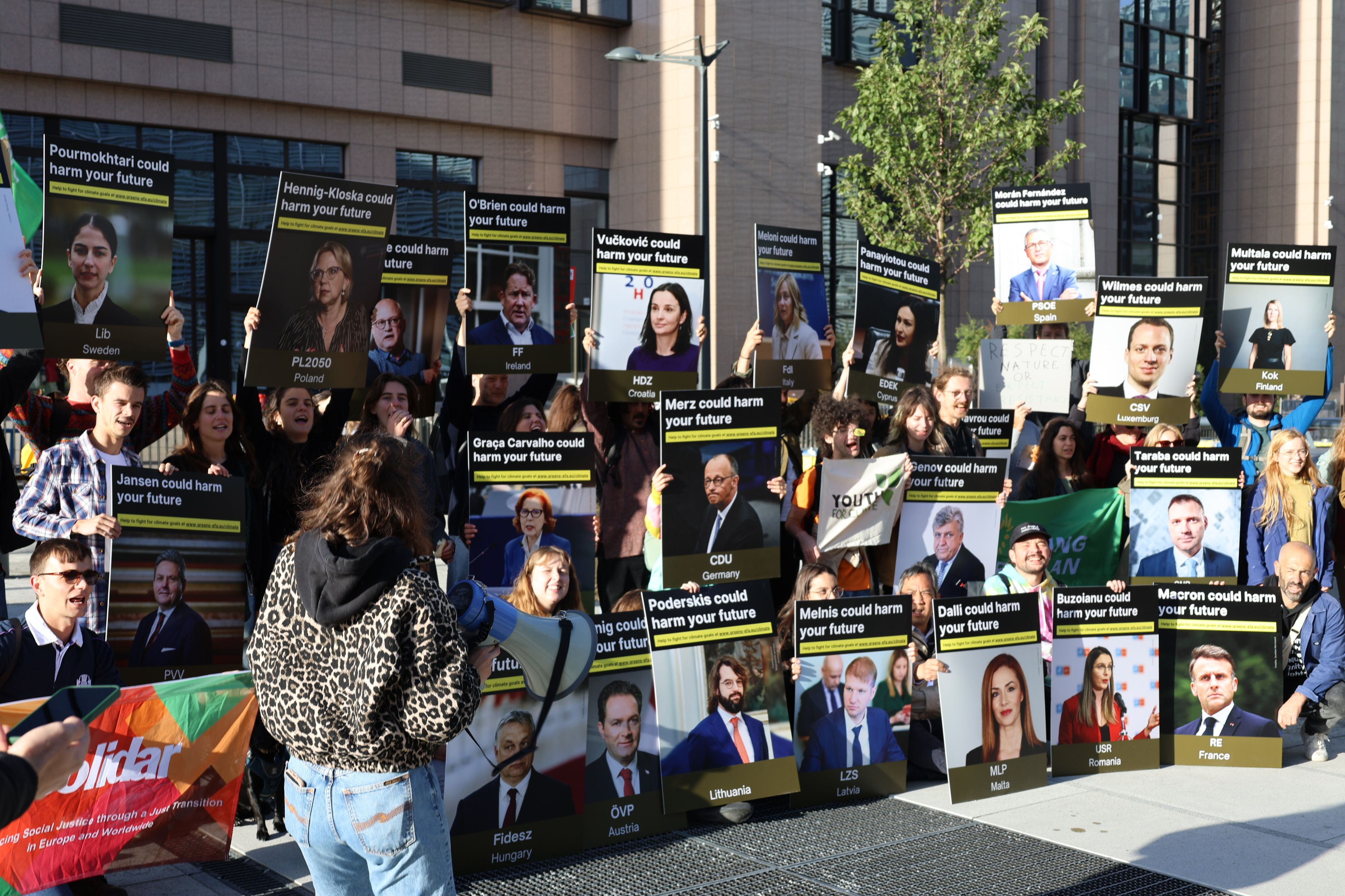 Activists and politicians standing in front of an EU building, holding signs ressembling the health prevention messages on cigarette packs with pictures of various European politicians from the right and far right parties, reading "this politician could harm your future". A Green MEP is standing in front of them with a megaphone.