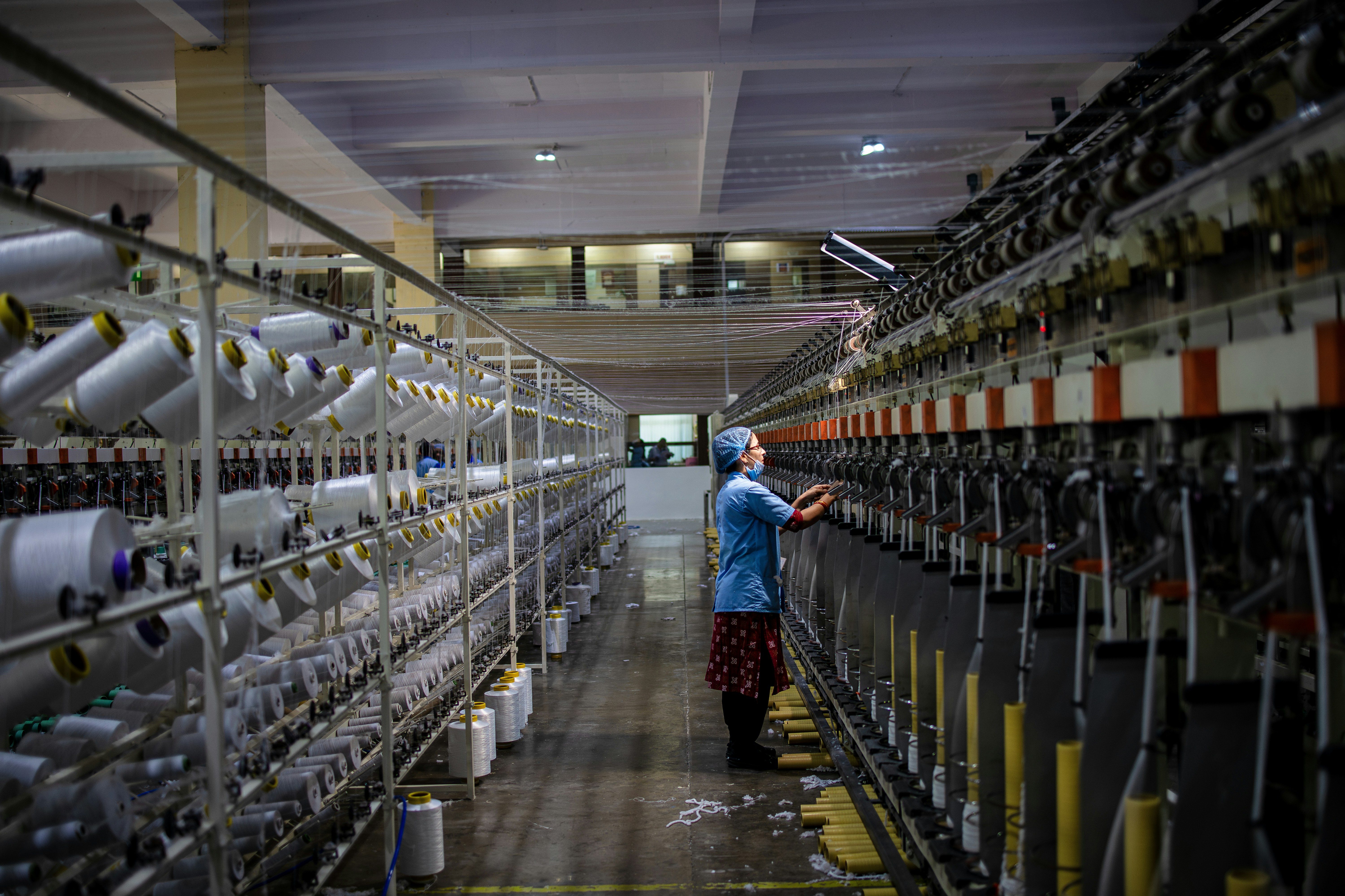 a factory worker in a blue unfirom with a mask and a head cover is working on industrial textile machines