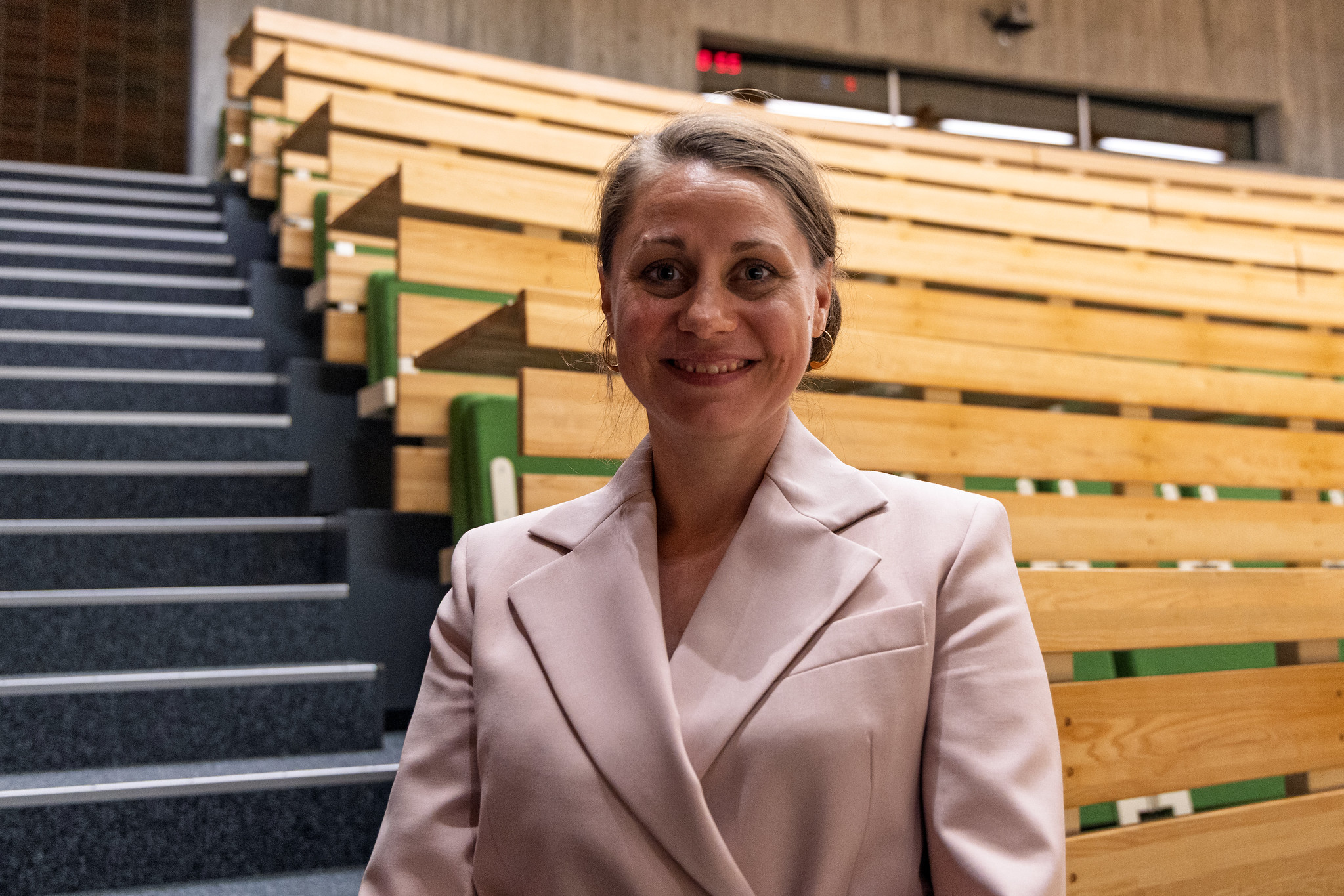 Sisse Marie Welling smiling in a pink suit, inside a building with stairs in the background