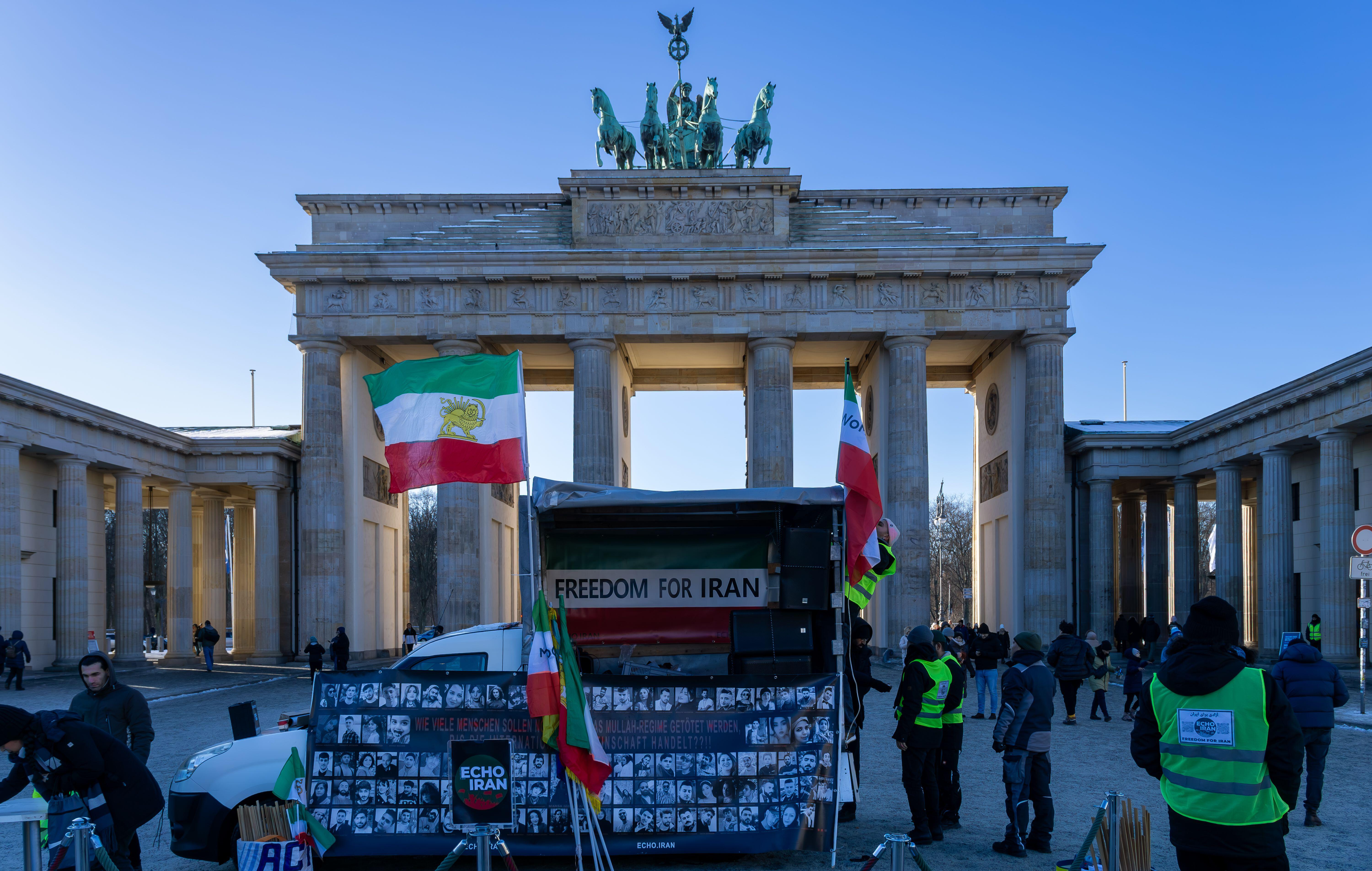 Peple standing in front of the Brandenburg Gate, with photos of regime victims and Iranian flags