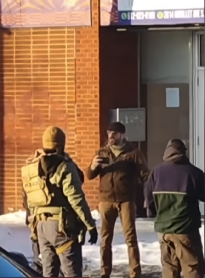 A man identified as Alex Pretti is holding a smartphone, standing in front of an ICE agent in the street