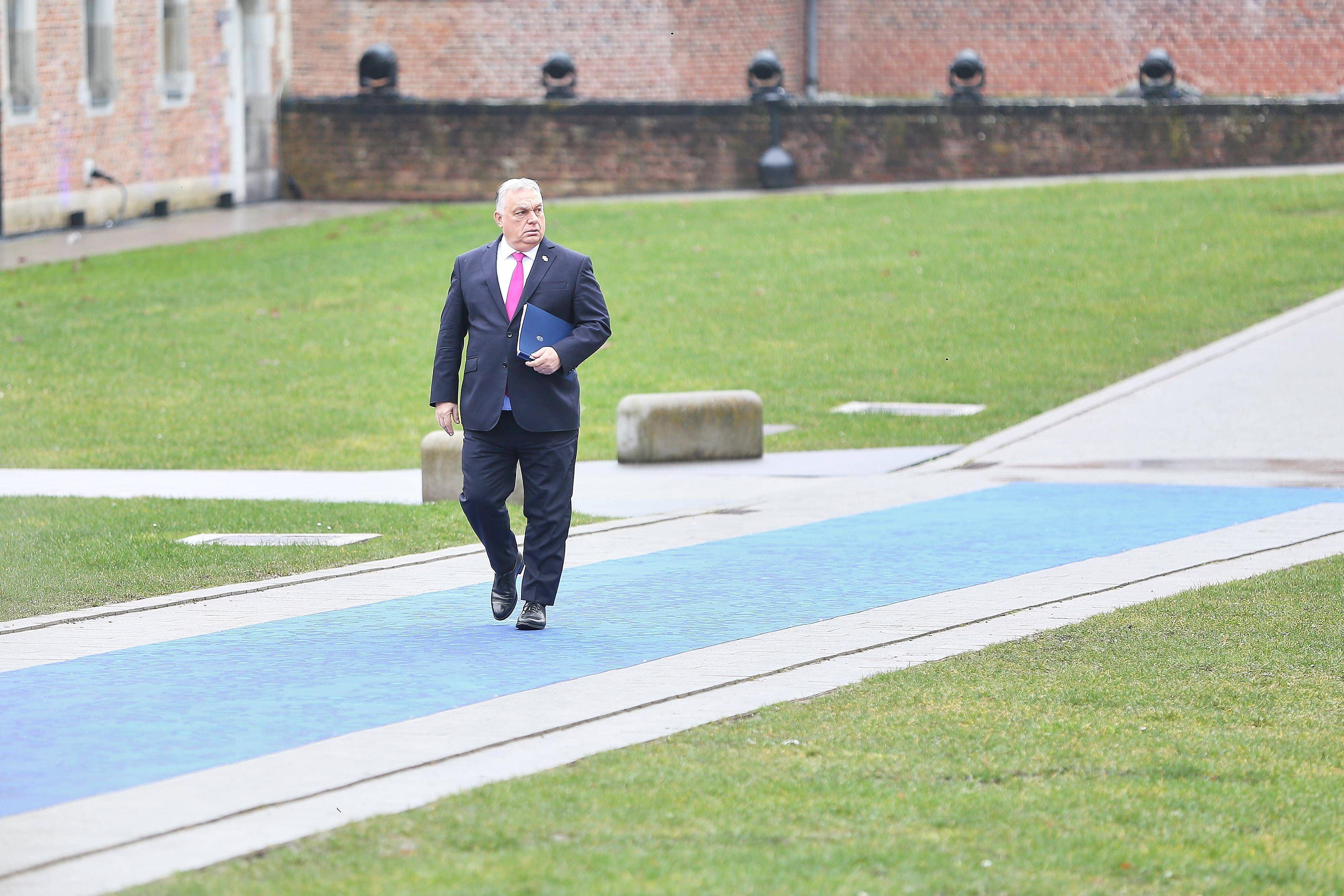 Viktor Orbán walking outside in a building garden, with a file under his arm on a blue carpet