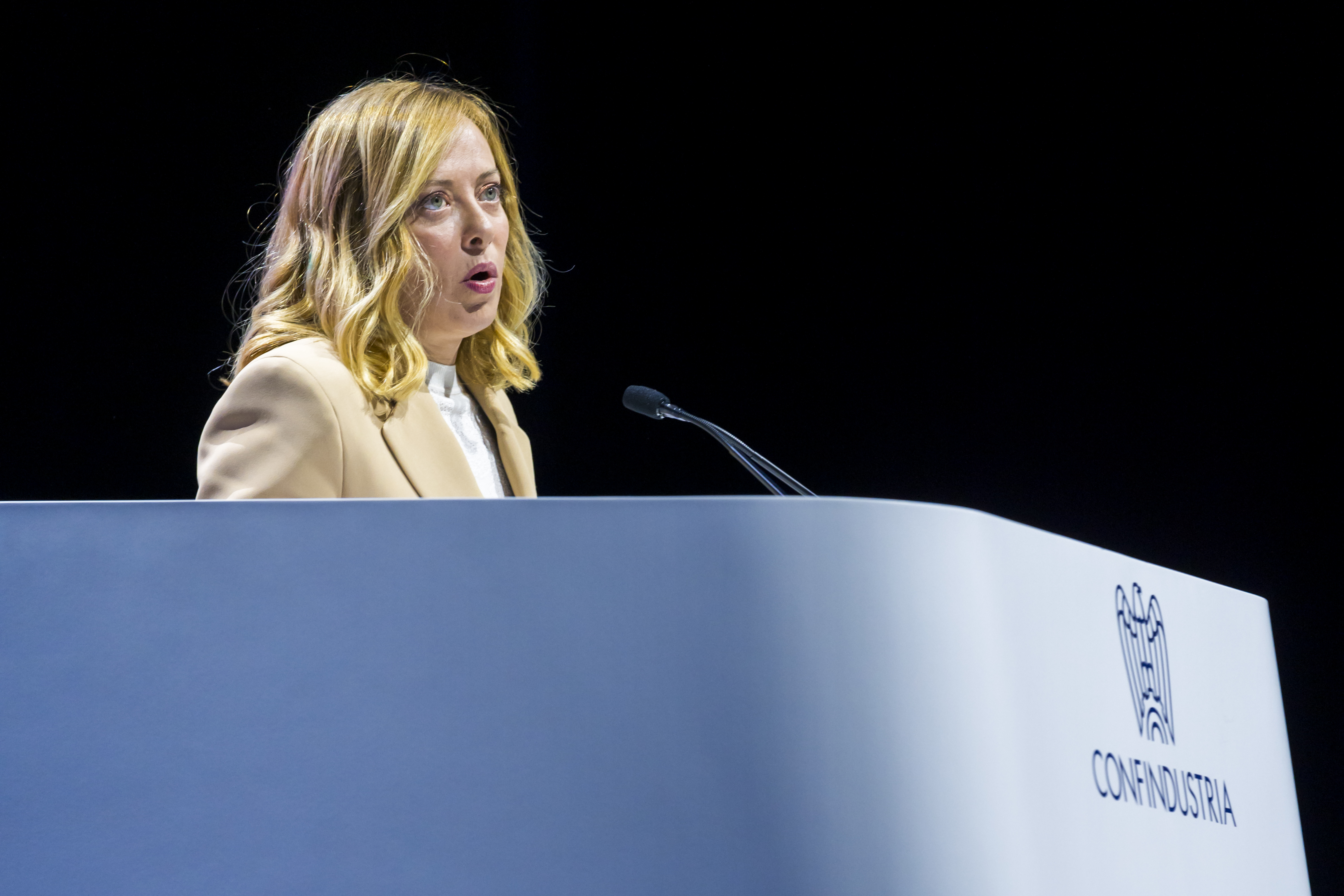 Georgia Meloni speaking in a mic at a conference, behind a lectern