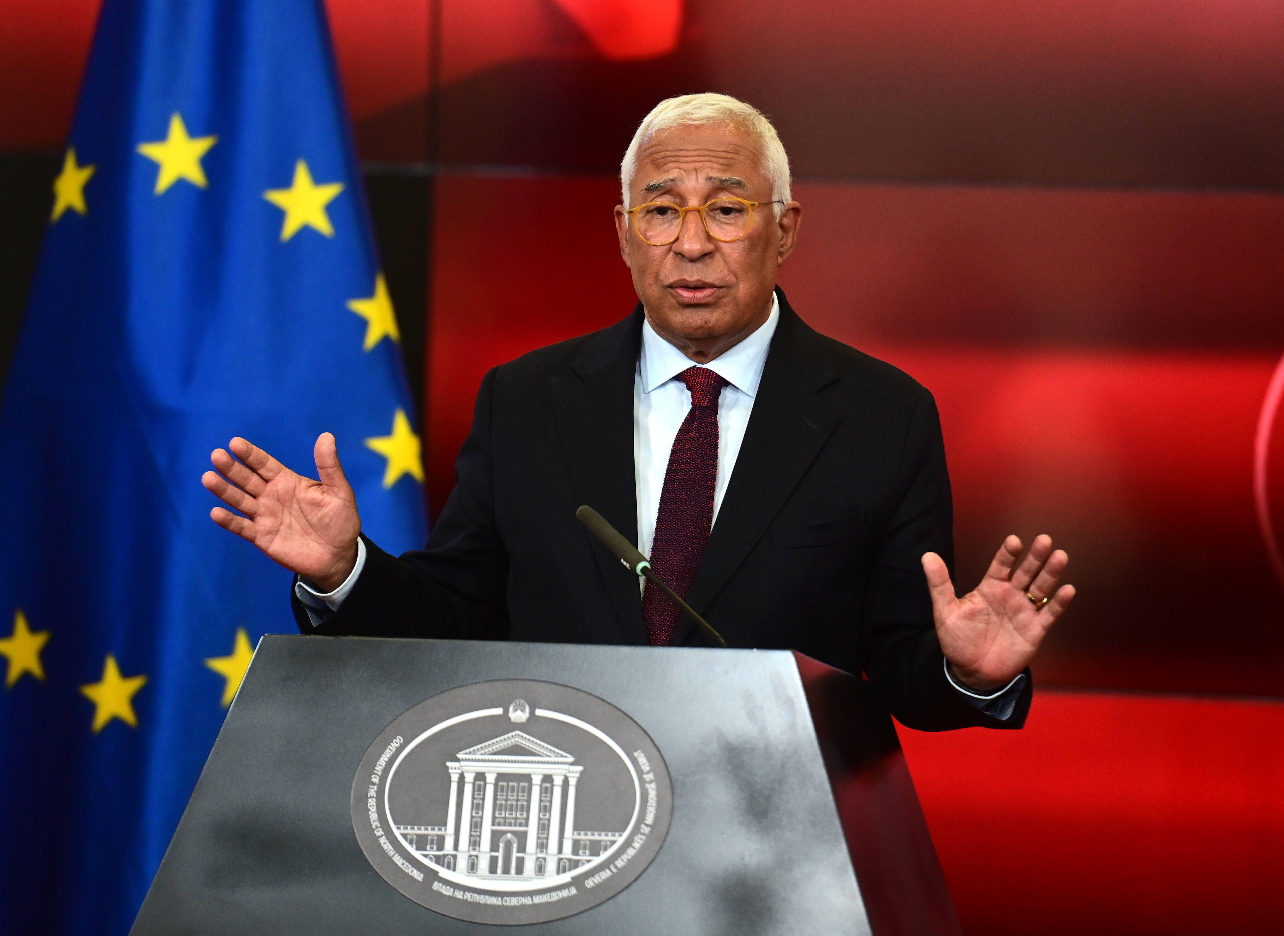 Antonio Costa, standing people a lectern with hands raised, on a red background with the European flag on his right.