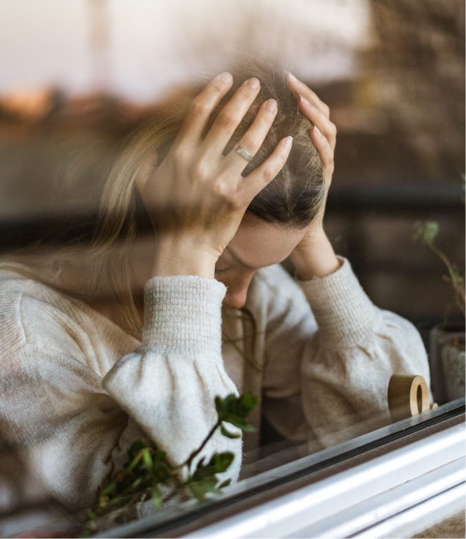 Woman with her hands on her head with her head against a window.
