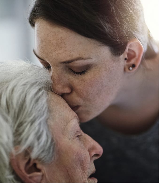 younger woman kissing the forehead of an older lady.