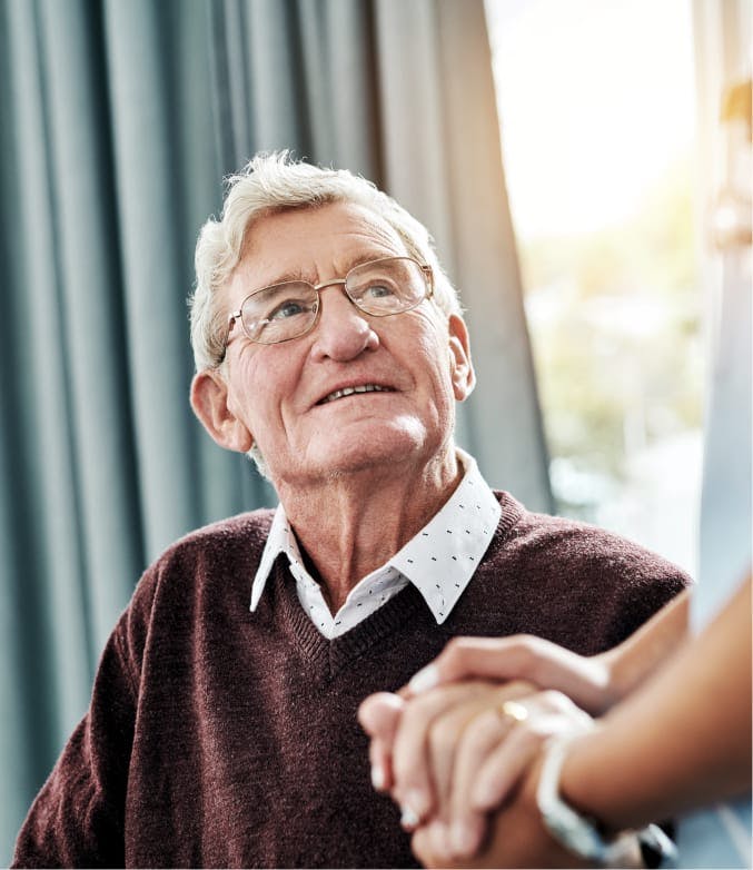 older man looking up at someone, his hand being held by another.