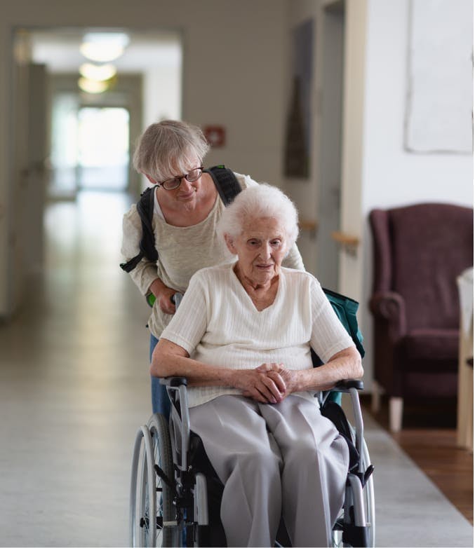 woman wheeling another older woman in wheel chair.