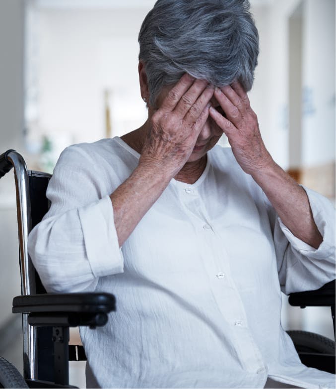 Older woman in a wheelchair with her head in her hands.