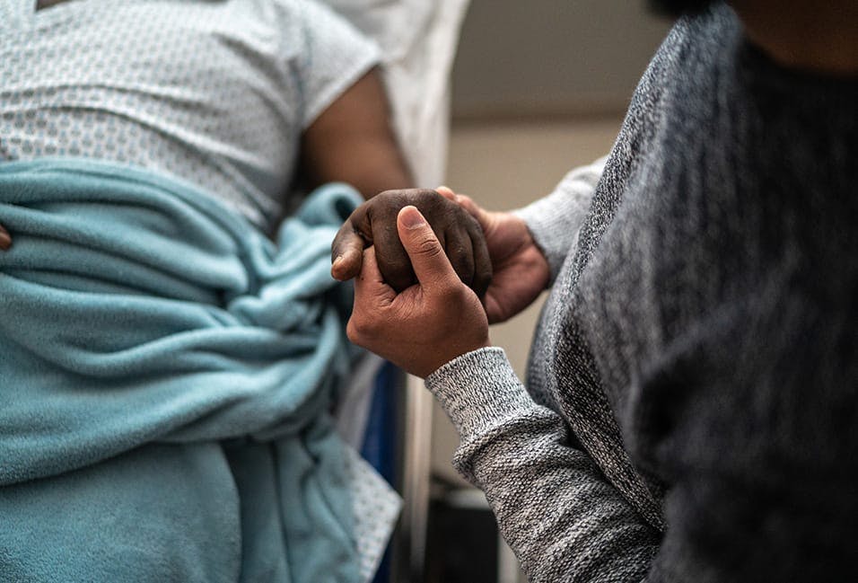 Person holding someones hand in a hospital bed