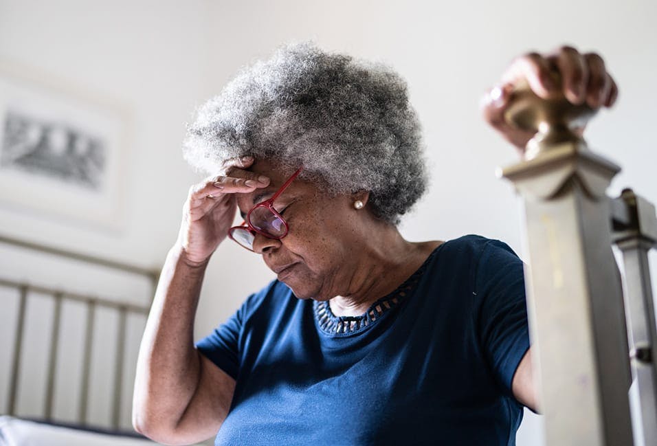 Elderly woman holding her head sitting on a bed