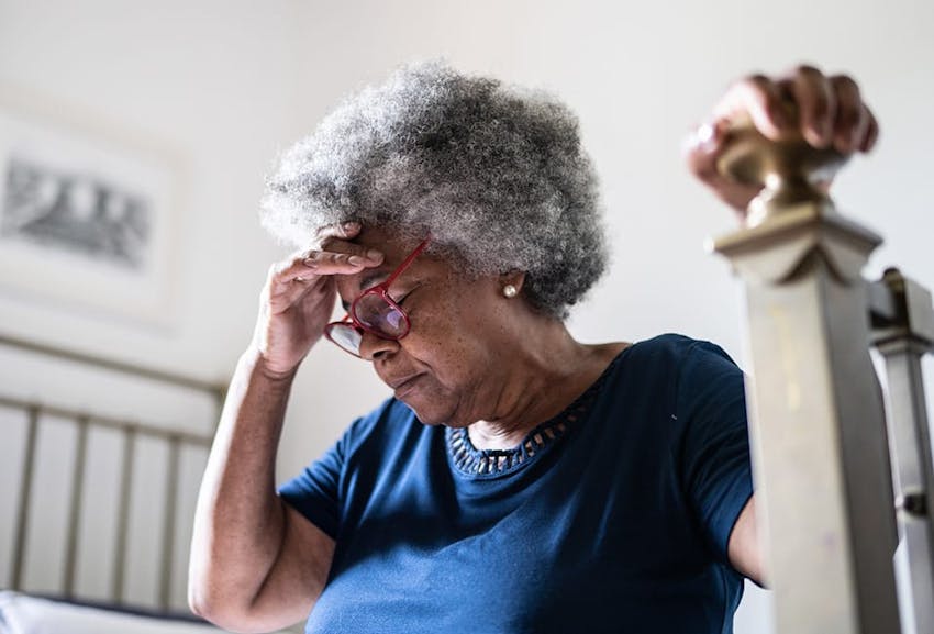 Elderly woman holding her head sitting on a bed