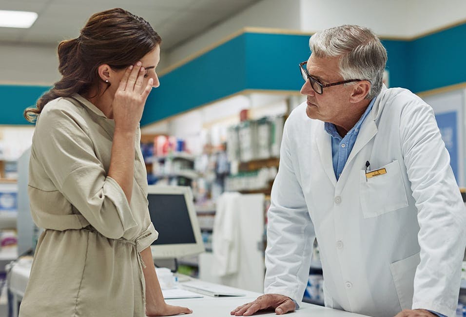 Woman holding her head talking to a pharmacist